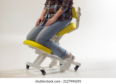 Woman is sitting on kneeling chair in office isolated on white. Ergonomic chair with wheels. Therapeutic stool with back support. Orthopaedic stool for desk based distance work from home.