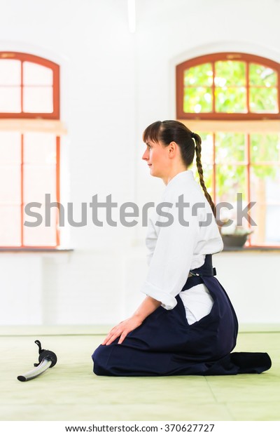 Woman sitting on mats while Aikido training in martial\
arts school 