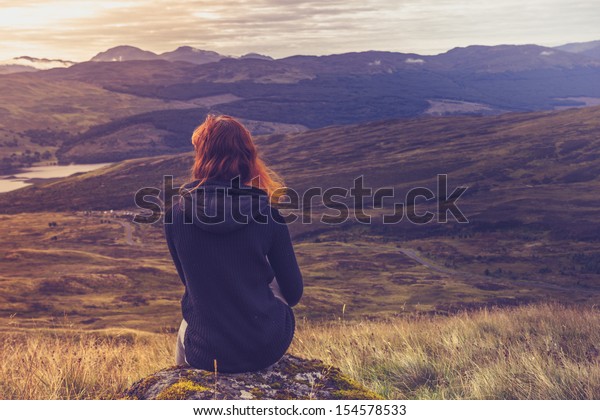 Woman sitting on mountain top and contemplating\
the sunset