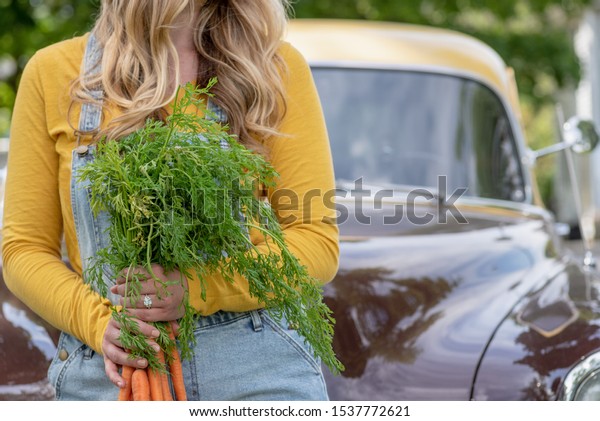 woman sitting on old truck holding bundle of\
organic carrots at farmers\
market