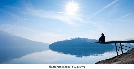 The Woman Is Sitting On The Pier. Self Reflection. Bright Sun In The Blue Sky.