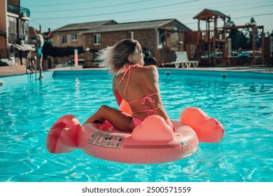 A woman is sitting on a pink flamingo float in a pool. The scene is bright and cheerful, with the woman enjoying her time in the water. - Powered by Shutterstock