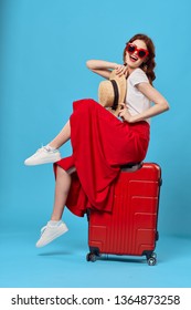  A woman is sitting on a red suitcase with her legs raised high and waiting for her flight on a plane                              