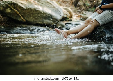 Woman sitting on the rock at waterfall, feet near the water surface