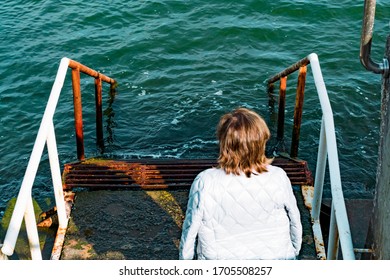 Woman sitting on the rusty staircase down in a sea water. Focus on the water and stairs - Powered by Shutterstock