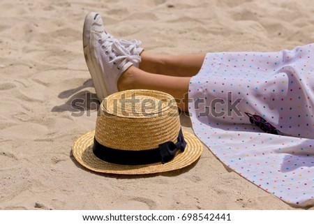 A woman sitting on a sandy beach only sees her feet and hats.