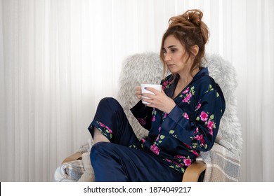 Woman Sitting On Sofa And Drinking Coffee, With Navy Nightgowns And Plush Slippers