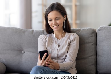 Woman sitting on sofa at home looks at smartphone device screen listens song choose online audio book make call or watching music videos. Teenage girl having fun spending free time in internet concept
