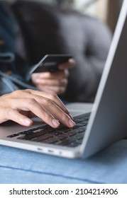 Woman Sitting On Sofa At Home, Hand Holding Credit Card And Using Laptop Computer For Internet Payment, Digital Banking And Online Shopping, E-commerce Concept, Closeup, Toned Image, Vertical