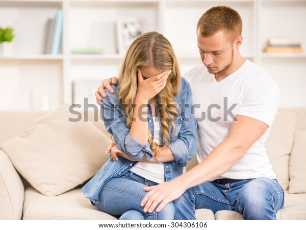 Mujer sentada en un sofá en casa y llorando mientras su marido la calva.