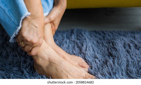 Woman Sitting On Sofa Using Hand To Hold Leg And Feeling Pain, Suffer, Hurt And Tingling. Concept Of Guillain Barre Syndrome And Numb Hands Disease Effect.