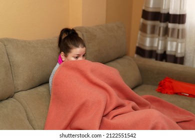 Woman sitting on the sofa wrapped in a blanket without heating