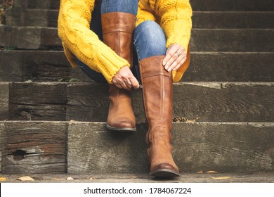 Woman sitting on stairs and fasten zipper on her leather boots. Autumn fashion concept