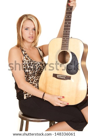 A woman sitting on a stool holding on to her guitar with a serious expression on her face.