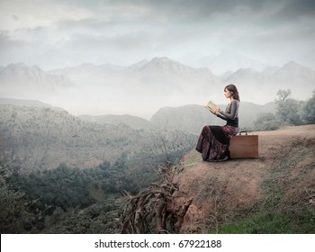 Frau sitzt auf einem Koffer und liest ein Buch mit Landschaft auf dem Hintergrund