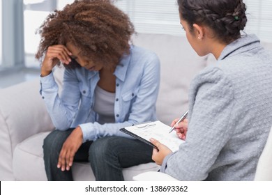 Woman Sitting On Therapists Couch Looking Down With Therapist Taking Notes