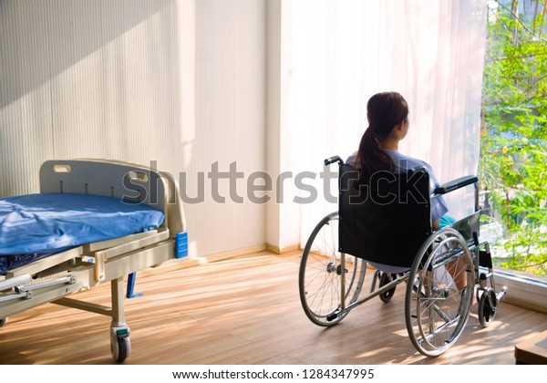 The woman sitting on wheelchair. She is see\
window with patient bed in hospital.disabled person lonely. Photo\
concept depression and\
Patient.