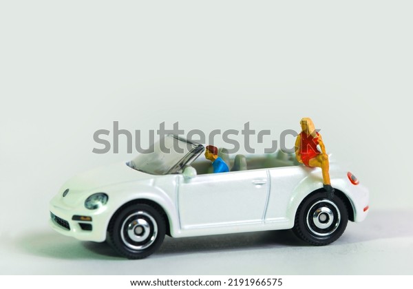 A woman is sitting on a\
white sports car cabriolet with driver, miniature figures scene,\
toy car