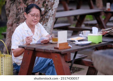 Woman sitting on a wooden bench in a garden restaurant, enjoying her afternoon ginger tea - Powered by Shutterstock