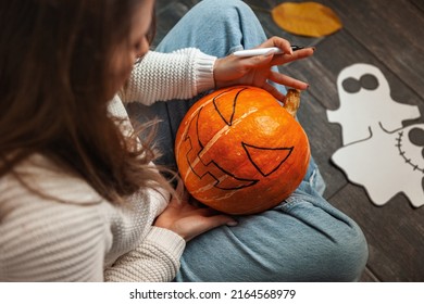 A woman sitting on a wooden floor painting a pumpkin face and makes Jack Latern for Halloween