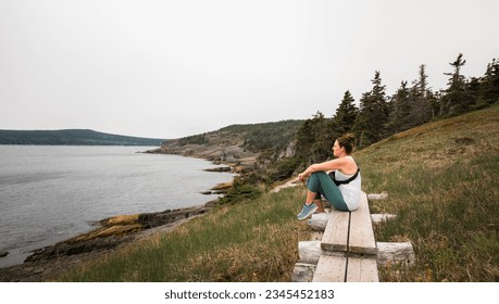 Woman sitting on wooden pathway looking at ocean on a hike. - Powered by Shutterstock