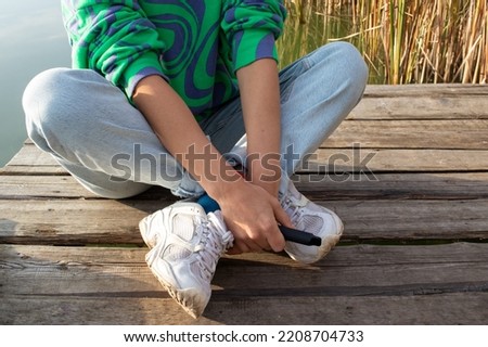 Woman sitting on the wooden pier over the river outdoors and holding e-cigarette in  hand before smoking. Heating tobacco system IQOS, iqos tobacco product technologies