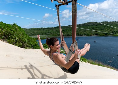 Woman Sitting On A Zip Line On Top Of A Dune Overlooking Jacomã Lagoon In The City Of Cerá Mirim-RN / Brazil.