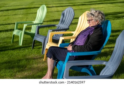 A Woman Sitting In One Of Five Adirondack Chairs On A Pretty Summer Day. Shadows.