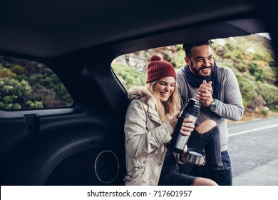 Woman sitting in the open car with coffee thermos flask and smiling. Couple having coffee break during their road trip. - Powered by Shutterstock