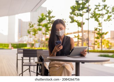 Woman Sitting Outdoors At Coffee Shop Restaurant Social Distancing And Wearing Face Mask To Protect From Covid 19 While Using Phone And Digital Tablet Horizontal Shot