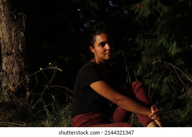 Woman Sitting Outdoors In Nature. The Ambience Is Dark And Moody And Half Her Face Is In Shadow. 