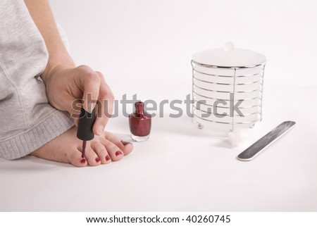 A woman sitting and painting her toes with her red finger nail polish.
