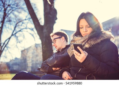 Woman Sitting In The Park With A Man And Using Smart Phone