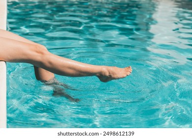 A woman is sitting in a pool with her feet in the water. Concept of relaxation and leisure - Powered by Shutterstock