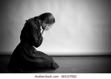 Woman Is Sitting In Profile On An Old Cracky Floor. She Is Sad And Depressed, Crying And Covering Her Face With Hands. Studio Paper  Background In Behing Her.