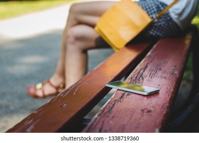 Woman Sitting In Public Park And Forget Smartphone On Bench. Lost Mobile Phone.