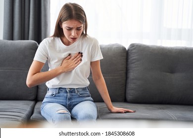 Woman sitting with strong chest pain and hands touching her chest while having trouble at home, Heart attack or heart failure symptom