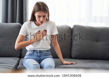Woman sitting with strong chest pain and hands touching her chest while having trouble at home, Heart attack or heart failure symptom