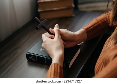 Woman sitting and studying the scriptures.The  wooden cross in the hands. Christian education concepts The Holy Scriptures open and pray to God. - Shutterstock ID 2234745327