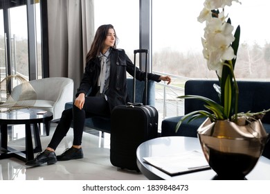 Frau sitzt mit Koffer in der Hotelhalle oder in einer Flughafenlounge