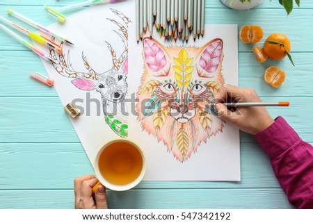 Woman sitting at table with coloring pictures for adults, closeup