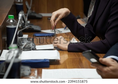 Woman, sitting at a table during a meeting or negotiations next to other people, holds a fountain pen. Businessman, lawyer or official. Photo. Selective focus. Unrecognizable. No face