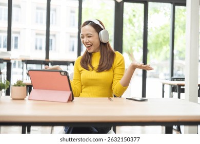 A woman is sitting at a table with a pink tablet and a cell phone. She is wearing headphones and she is listening to music. The scene suggests a relaxed and leisurely atmosphere