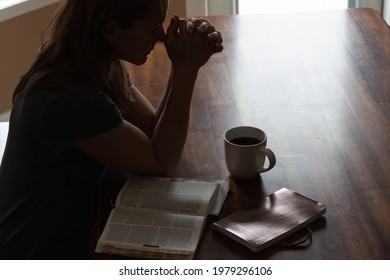 Woman sitting at table praying with open bible and cup of coffee - Powered by Shutterstock