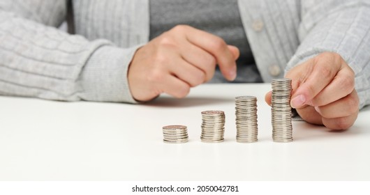 Woman Is Sitting At The Table And A Stack Of Coins On The Table. Calculation Of Expenses And Income, Subsidy, Tax