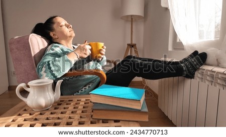 Woman sitting in the toom, drinking tea on a cold winter day outside.