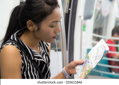 Woman Sitting In A Train And Is Studying The Route Map. Asian Tourist In Wagon Of Metro Is Looking At City Transport Plan Singapore. The Traveler In The Subway.