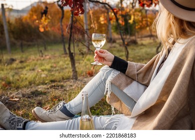 Woman Sitting In Vineyard And Drinking White Wine. Relaxation In Fall Winery After Grape Harvesting