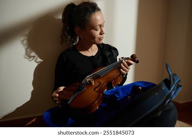 A woman sitting with a violin, appearing in thoughtful contemplation. The scene reflects a moment of quiet introspection and musical connection, accompanied by soft lighting and a serene mood. - Powered by Shutterstock