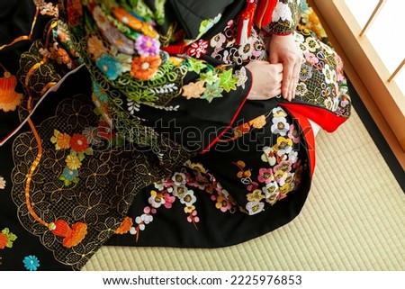 A woman sitting wearing a twelve-layered ceremonial kimono